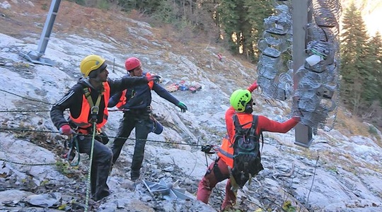 Drei Personen mit Schutzkleidung in gebirgigem Gelände